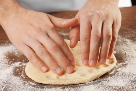 Hands preparing dough basis for pizza on the wooden table, close-upの写真素材