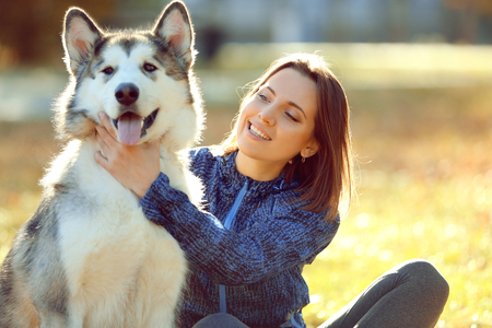 Happy young woman sitting with her dog on grass in parkの写真素材
