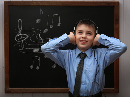 Young cute schoolboy wearing headphones at the blackboard with musical notes