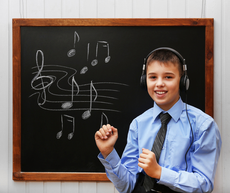 Young cute schoolboy wearing headphones at the blackboard with musical notesの写真素材