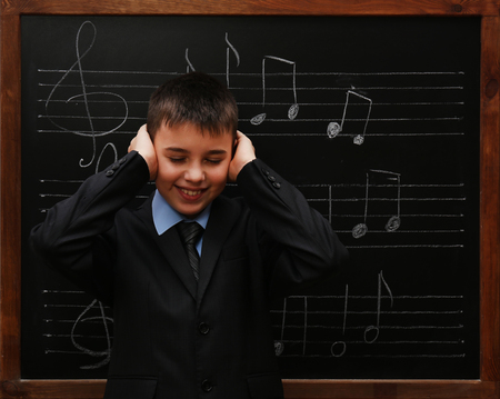 Young cute schoolboy standing at the blackboard with musical notesの写真素材