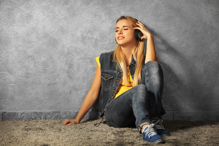Young woman sitting on the floor and listening to music on a grey wall backgroundの写真素材