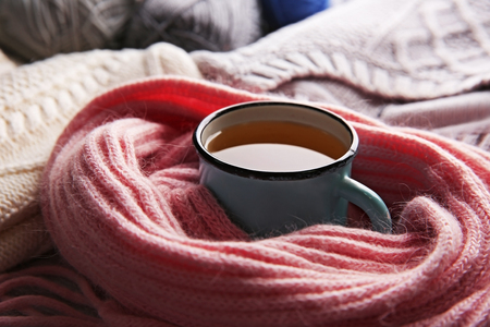 Mug of tea wrapped in scarf and warm clothes beside it closeupの写真素材