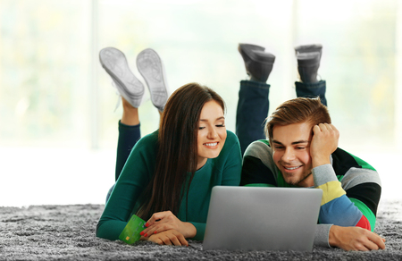 Young happy couple using credit card with laptop at home on light backgroundの写真素材
