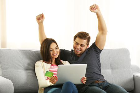Young happy couple using credit card with laptop at home on light backgroundの写真素材