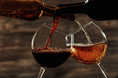 White and red wine pouring in glasses on wooden backgroundの写真素材