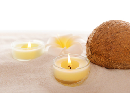 Coconut with plumeria and candles on sand, isolated on whiteの写真素材