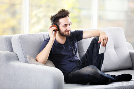 Handsome man emotionally listens music with headphones on grey sofa in the roomの写真素材