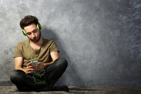 Young bearded man listens music with headphones sitting on grey wall backgroundの写真素材