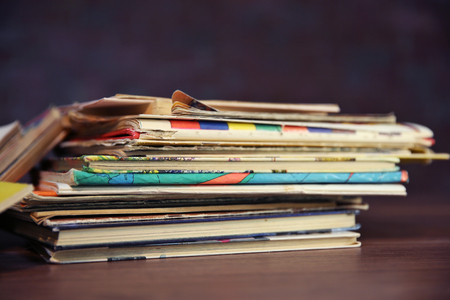 Pile of old books on wooden table against brick wall, close upの写真素材