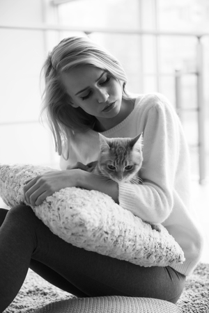 Black-and-white photo of attractive young woman playing with red cat on the floorの写真素材