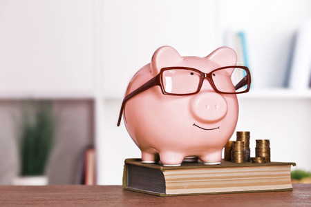 Piggy bank in glasses with book and coins on home or office backgroundの写真素材