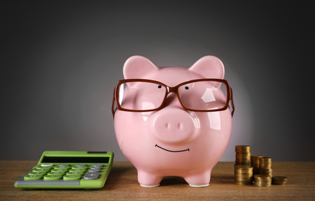 Piggy bank in glasses with calculator and coins on grey backgroundの写真素材