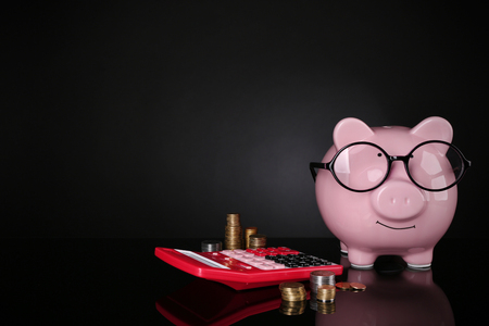 Piggy bank in glasses with calculator and coins on dark backgroundの写真素材