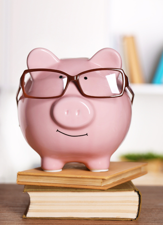Piggy bank in glasses with books on home or office backgroundの写真素材