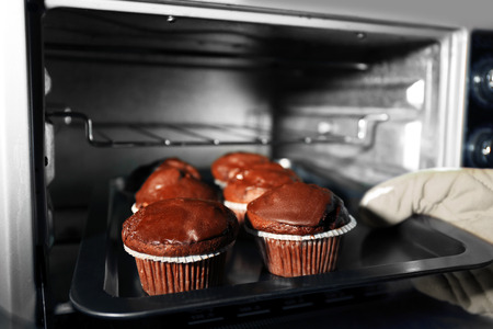Housewife preparing chocolate cupcakes in oven, close upの写真素材