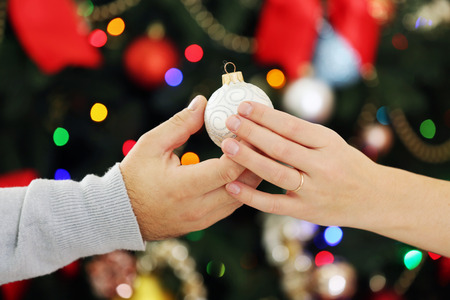 Female and male hands with Christmas bauble on bright backgroundの写真素材