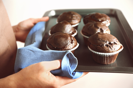 Housewife holding oven-tray with chocolate cupcakes, close upの写真素材