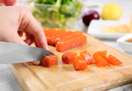 Woman cutting smoked salmon for salad, at kitchenの写真素材