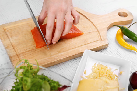 Woman cutting smoked salmon for salad, at kitchenの写真素材