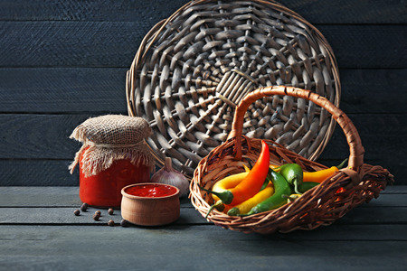 Chili peppers in wicker basket and homemade sauce salsa on  wooden backgroundの写真素材