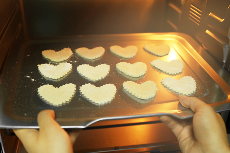 Uncooked heart shaped biscuits on a baking tray in an ovenの写真素材