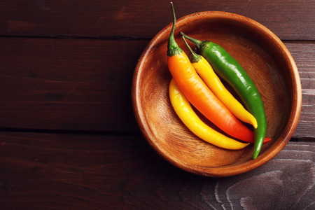 Colorful chili peppers in bowl on dark wooden backgroundの写真素材