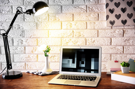 Modern lamp and laptop on table on brick wall backgroundの写真素材