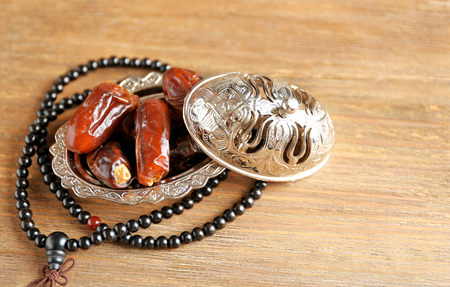 Composition of dried dates in holiday dish and rosary on wooden backgroundの写真素材