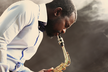 African American jazz musician playing the saxophone against smoky backgroundの写真素材
