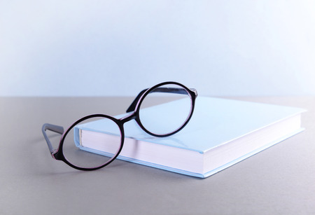 Books and eyeglasses on grey table against blue wallの写真素材