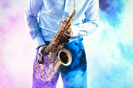 African American jazz musician playing the saxophone against colorful smoky backgroundの写真素材