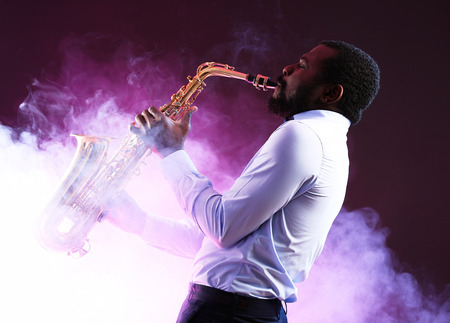 African American jazz musician playing the saxophone against colorful smoky backgroundの写真素材