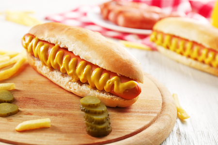 Hot dog with fried potatoes and cucumber on wooden cutting board closeupの写真素材