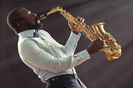 African American jazz musician playing the saxophone on grey backgroundの写真素材