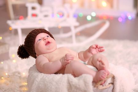 Adorable baby in brown knitted hat in decorated wicker basketの写真素材