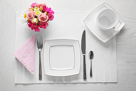 Table setting with dishes, cutlery and flowers on white backgroundの写真素材