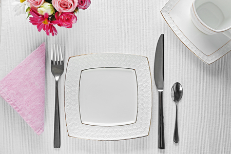 Table setting with dishes, cutlery and flowers on white backgroundの写真素材