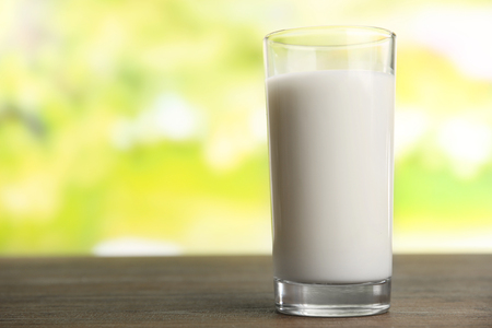 Glass of milk on table on blurred natural backgroundの写真素材