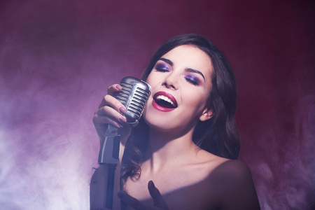 Beautiful singing woman on red background in the smoke, close upの写真素材