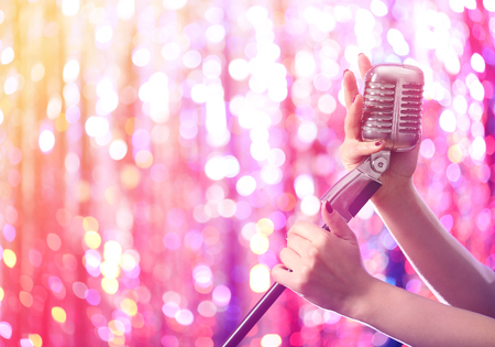 Female hands holding microphone against bright glitter backgroundの写真素材