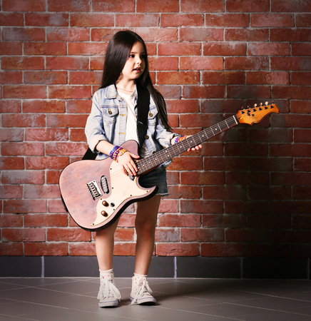 Beautiful little girl with guitar on brick wall backgroundの写真素材