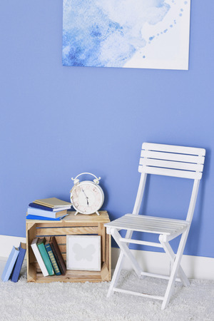 Room design with white chair, bookcase and picture over blue wallの写真素材