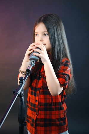 Beautiful little girl with microphone on dark purple backgroundの写真素材