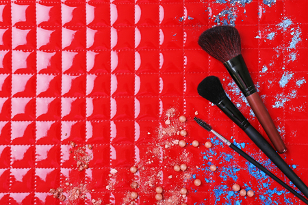 Three makeup brushes with drops of shadows and rouge on red backgroundの写真素材