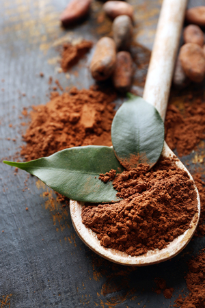 Spoon with aromatic cocoa powder and green leaf on scratched wooden background, close upの写真素材