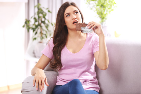 Portrait of beautiful young brunette with chocolate on sofa in the room , close up