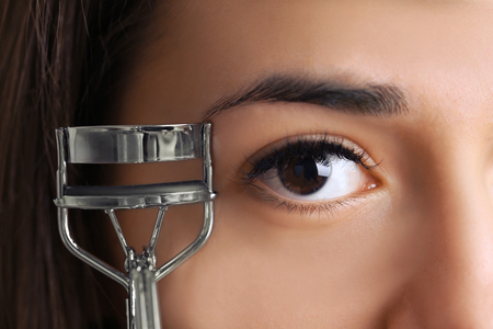 Woman corrects eyelashes with curling tongs, close upの写真素材