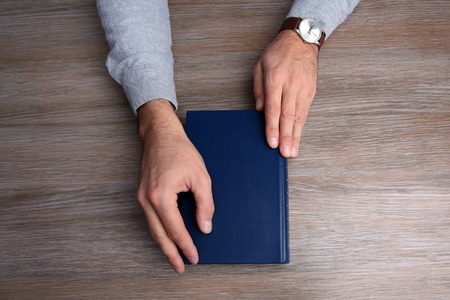 Man hands holding book, on wooden table backgroundの写真素材