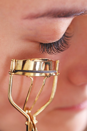 Woman corrects eyelashes with curling tongs, close upの写真素材